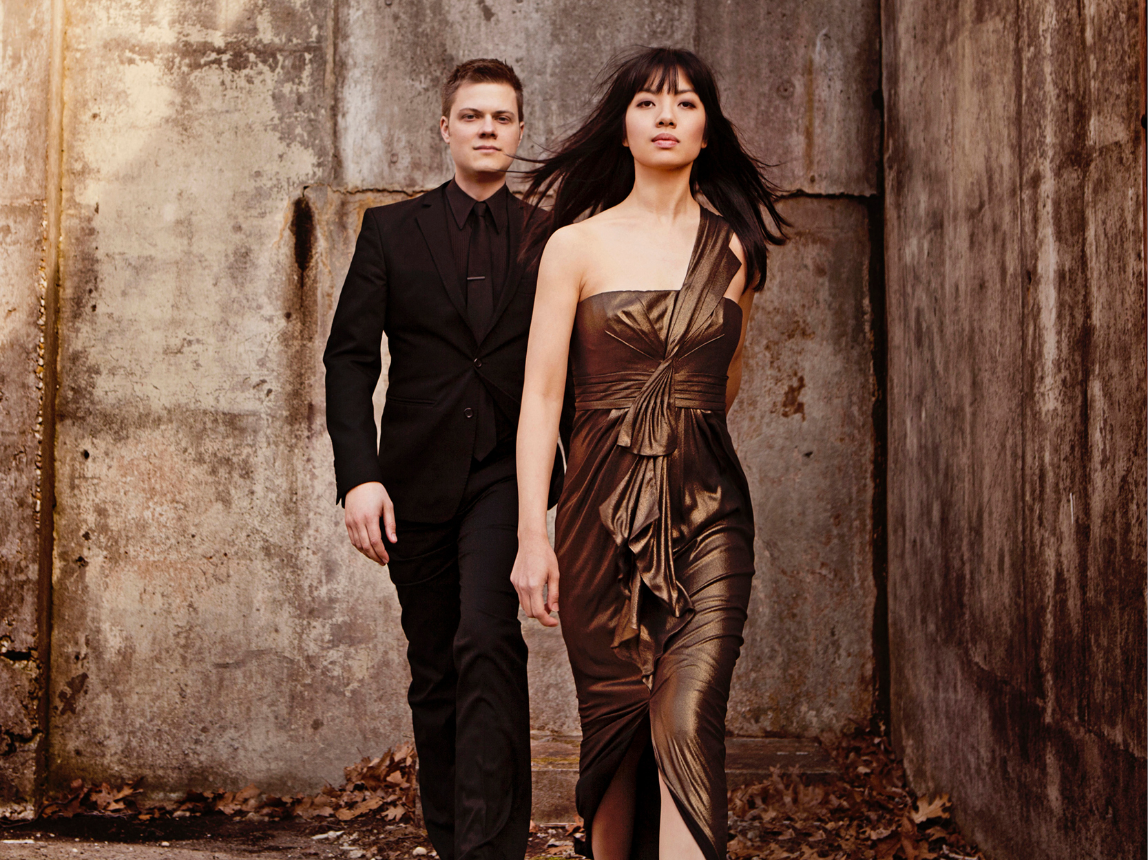 A man and a women by a cement building. They are dressed up.